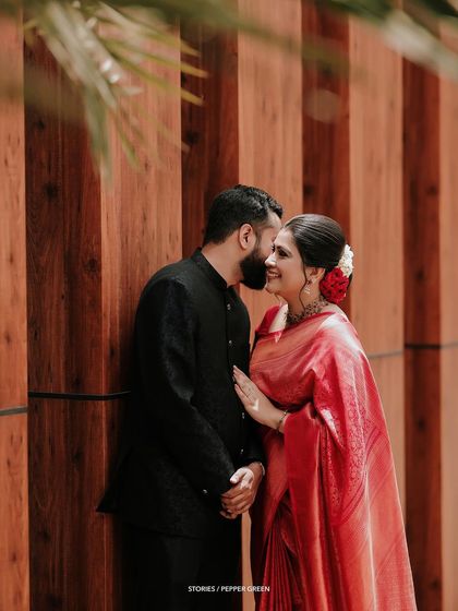 A sweet, stolen moment between Jesna and Antony. The rich red of her saree against the warm wood tones creates a visually stunning and romantic image.