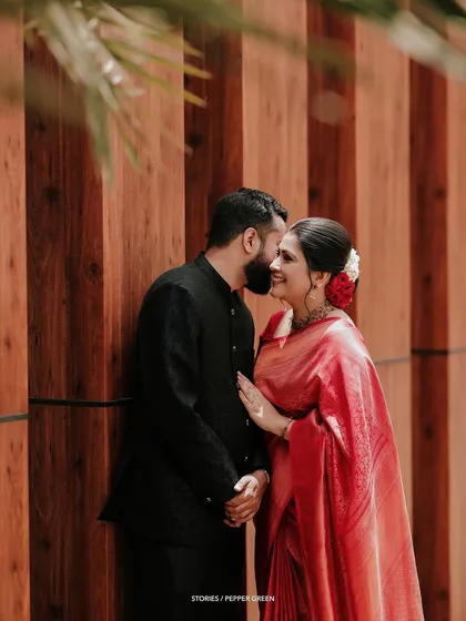 A sweet, stolen moment between Jesna and Antony. The rich red of her saree against the warm wood tones creates a visually stunning and romantic image.