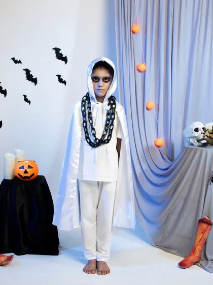 A child in a spooky ghost costume with a white cape and chain necklace.