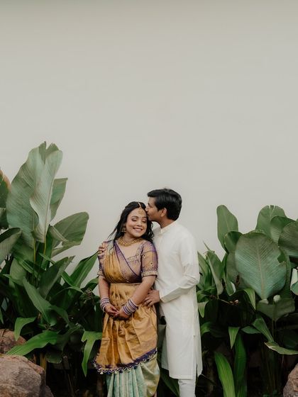 A tender moment from a pre-wedding shoot. The groom kisses the bride's forehead as she smiles, their simple white outfits adding to the pure and gentle feel of the image.