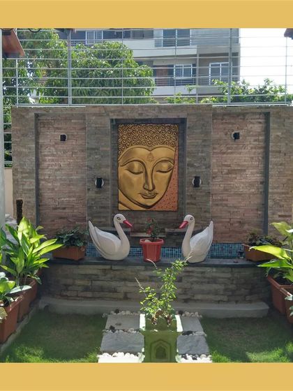 A tranquil garden space from the Hemavathi and Hareesh residence, featuring a stone wall with a serene Buddha mural, creating a peaceful outdoor sanctuary.
