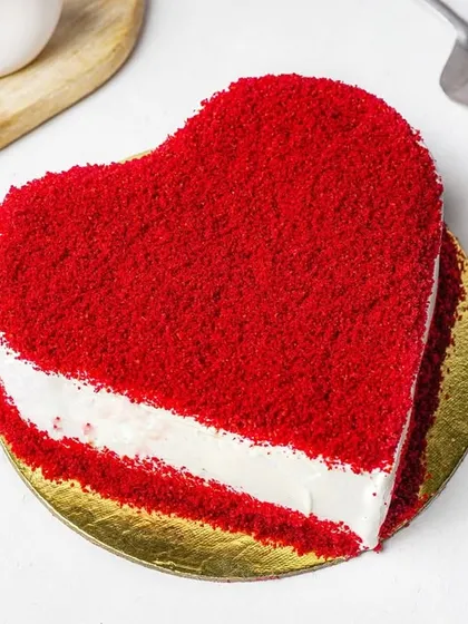 A vibrant red velvet heart-shaped cake, shot from above with a cake server and whisk. This styled shot is perfect for Valentine's Day, anniversaries, or other special promotions.