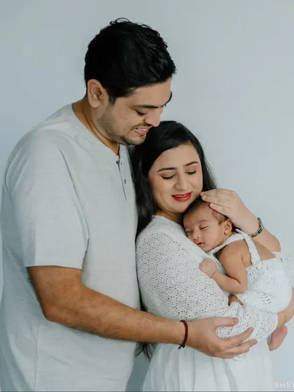 Dressed in coordinating white outfits, this family of three radiates peace and love. The mother cradles her sleeping newborn while the father wraps his arms around them, creating a portrait of pure serenity.