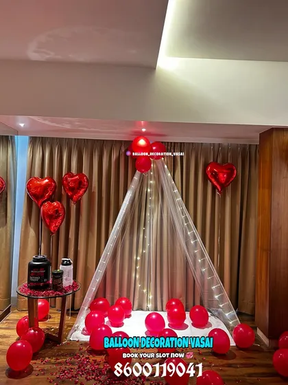 For a cozy and cute surprise, I can set up an indoor canopy tent. This romantic corner is decorated with sheer white fabric, fairy lights, red balloons, and scattered rose petals, creating a perfect little hideaway for a special evening.
