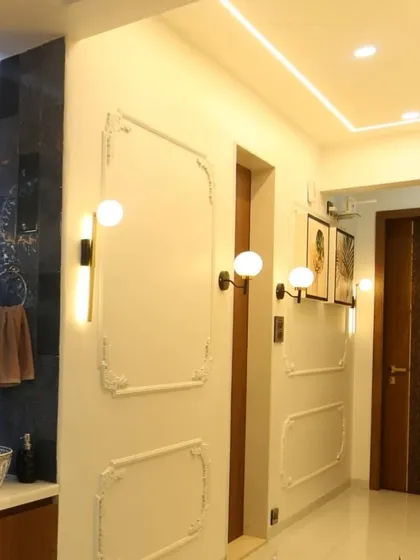 This view shows the passage leading from the wash basin area, featuring classic wall mouldings and modern globe wall lights that create a warm and inviting pathway through the home.