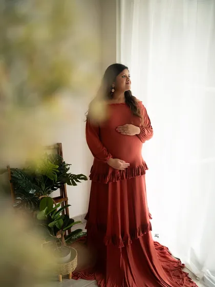 Bathed in beautiful window light, this mother-to-be looks serene in a lovely rust-colored ruffled gown, creating a warm and earthy portrait.