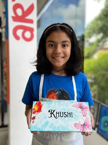 A young participant proudly displays the personalized nameplate she made in our decoupage workshop. These sessions are great for kids, allowing them to create a custom piece for their room.
