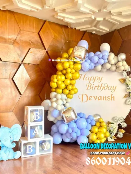 Celebrating a first birthday is a huge milestone. This setup for Devansh's birthday features a personalized backdrop, a stylish balloon arch in blue, yellow, and silver, and transparent "BABY" blocks for a fun photo corner.
