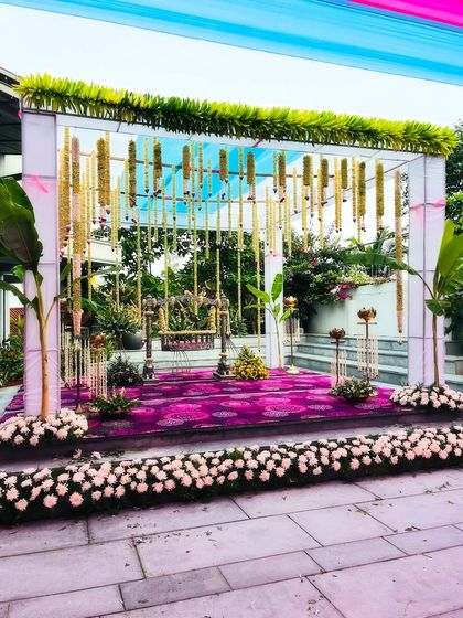 An elegant outdoor setup for a naming ceremony. The stage features a decorated cradle under a modern canopy with hanging floral garlands, blending traditional and contemporary styles.