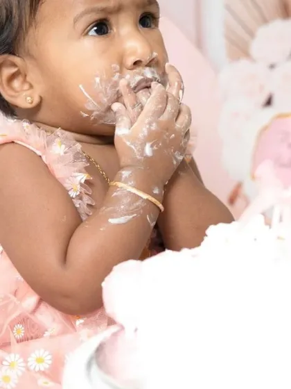A sweet one-year-old girl enjoying her pink-themed cake smash session. I love capturing these close-ups of their frosting-covered fingers and happy faces.