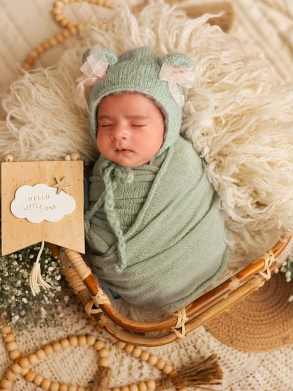 "Hello Little One." A newborn sleeps in a basket next to a sweet wooden sign, a lovely detail for a birth announcement photo.