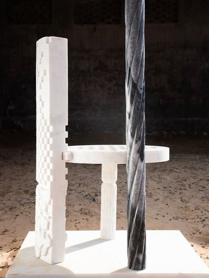 The Dori Patti chair, seen here from a different angle, reveals the twisted black marble pillar contrasting with the carved white marble. This piece is a dialogue between different materials, textures, and forms.