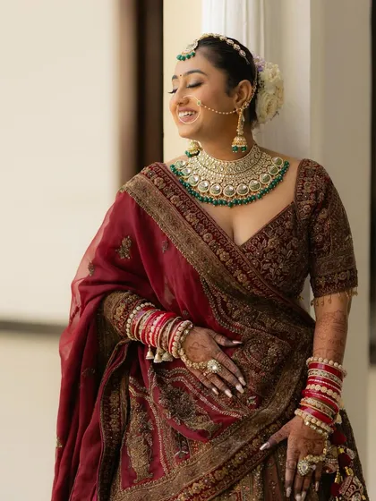 A candid portrait of the bride, Anjani, sharing a moment of pure laughter. Her stunning green and gold jewelry and traditional attire are beautifully captured.