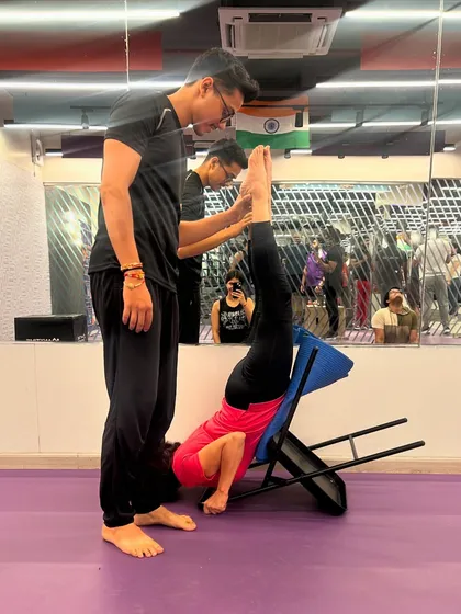 Assisting a student with a supported inversion using a chair. This is a safe way to experience the benefits of being upside down, such as improved circulation and reduced stress.