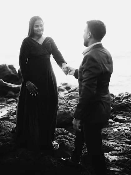 A moody black and white shot of a couple on a rocky shore. The dramatic landscape and their connected hands create a powerful, story-driven image.