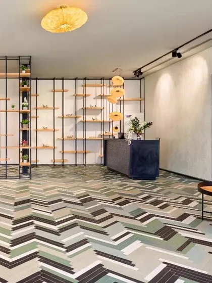 A lobby featuring a bold, geometric-patterned floor and open metal-and-wood shelving. This design creates a vibrant, contemporary, and slightly industrial feel.