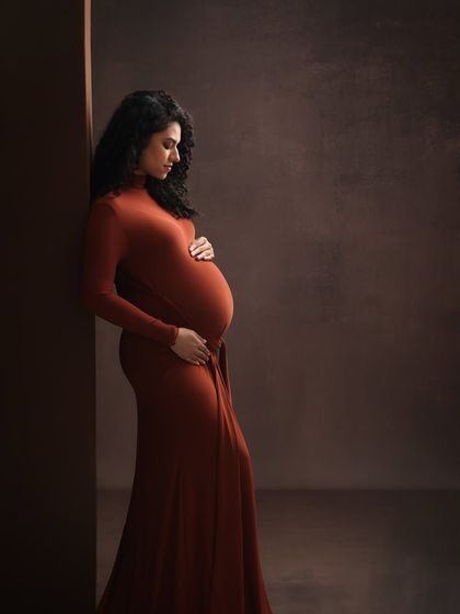 A profile of strength and grace. This portrait uses shadows and a rich, rust-colored gown to sculpt a beautiful and timeless image of the expectant mother.