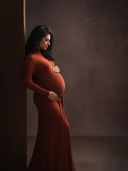 A profile of strength and grace. This portrait uses shadows and a rich, rust-colored gown to sculpt a beautiful and timeless image of the expectant mother.