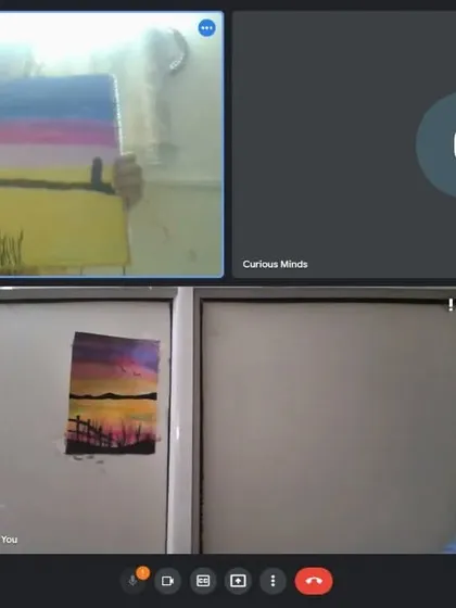 A student in an online class holding up his sunset landscape painting, with my example on the screen for reference.