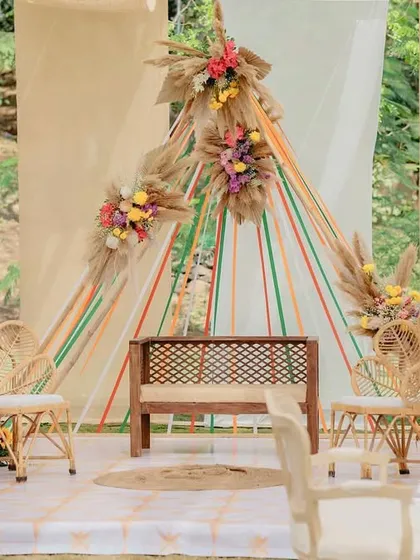 The main seating area for a boho-chic Mehendi, featuring a backdrop of colorful ribbons, pampas grass, and vibrant floral arrangements.
