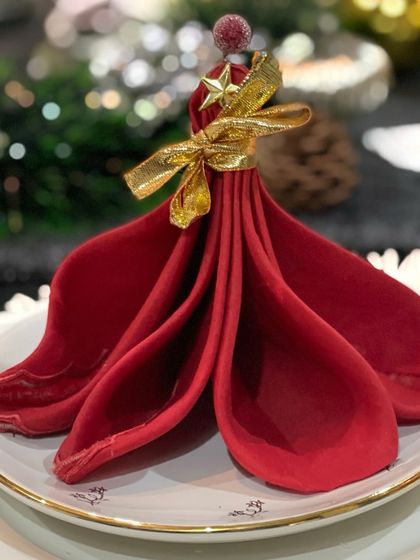 A festive Christmas napkin fold to bring holiday magic to your feast. This red napkin is folded to resemble a charming Christmas tree, complete with a gold ribbon and a star.