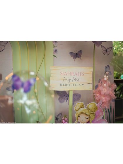 A detailed view of the "Siahran's Fairy First Birthday" sign, set against a butterfly-print backdrop. The soft focus on the foreground balloon adds to the dreamy quality of the decor.