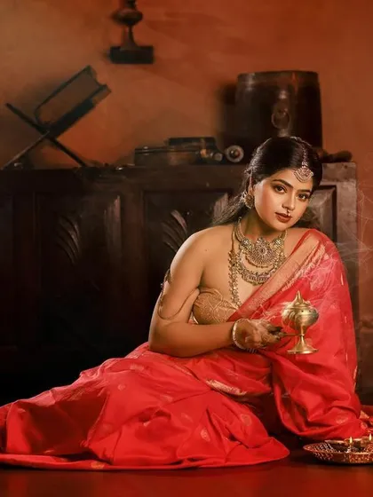 This full-length portrait captures the bride seated in a classic pose, holding a brass vessel. The composition and lighting are designed to evoke the feeling of an old-world oil painting, rich in detail and emotion.