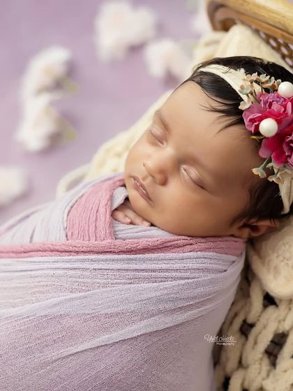 A close-up portrait of the newborn girl, highlighting the beautiful floral headband and her peaceful, sleeping face.