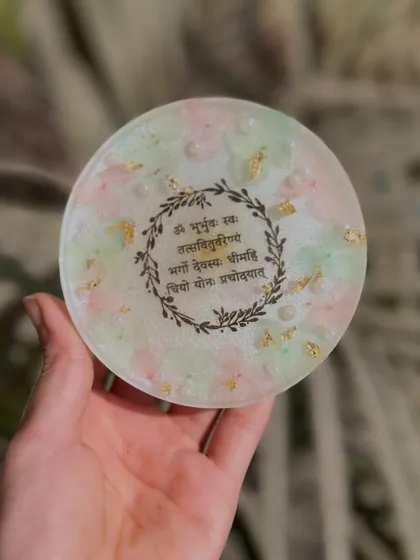 A beautiful coaster featuring the Gayatri Mantra, surrounded by a delicate floral wreath design. Perfect for your daily moment of peace.
