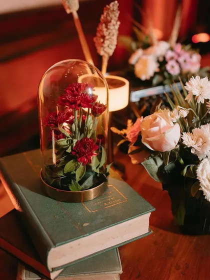 A close-up of a centerpiece detail, with red flowers preserved under a glass cloche on a stack of old books.