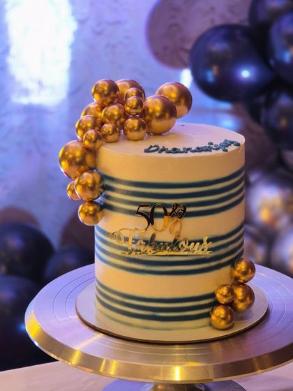 A close-up of a 50th birthday cake with blue stripes and a cascade of golden baubles. It's a modern and celebratory design.