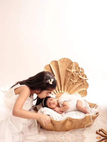 An older sister gently kisses her newborn sibling, who is resting in a golden seashell prop. This is a precious moment that perfectly captures the beginning of a lifelong sibling bond.