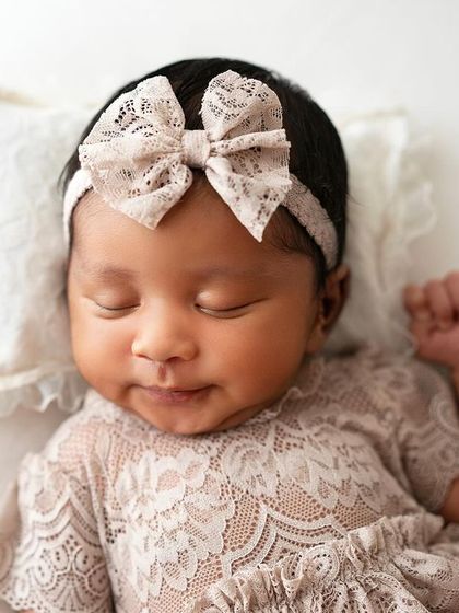 A close-up on this adorable little face, resting on a tiny pillow. The lace outfit and headband are so delicate and sweet.