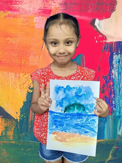 A young artist gives a peace sign as she holds her watercolor seascape, a beautiful and atmospheric piece.