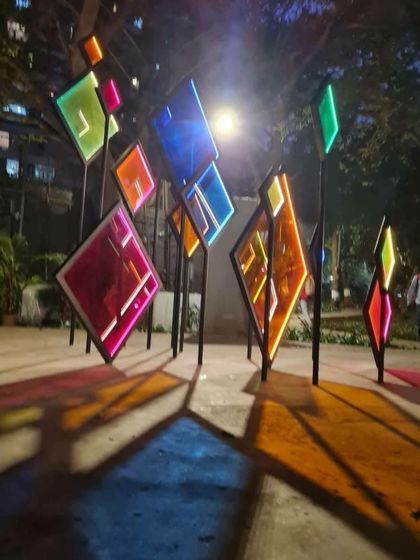 The 'Family Tree' installation illuminated at night, casting colorful shadows on the ground. The design considers both the daytime and nighttime experience, ensuring the artwork is a vibrant presence around the clock.