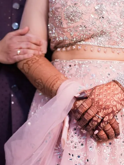 A close-up shot focusing on the couple's hands and the bride's beautiful lehenga.