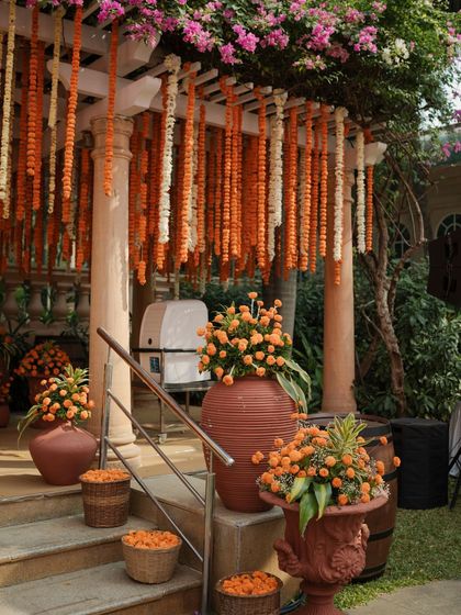 The entrance to the Haldi ceremony, decorated with cascading marigold strings and large terracotta vases filled with orange blooms.