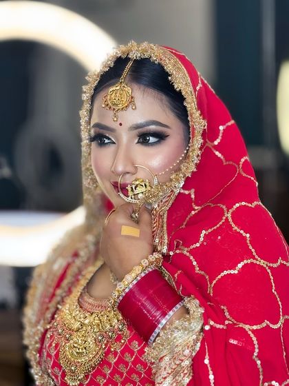 A close-up profile shot of a bride in red. The ring light in the background highlights her flawless HD makeup and the intricate details of her dupatta and jewelry.