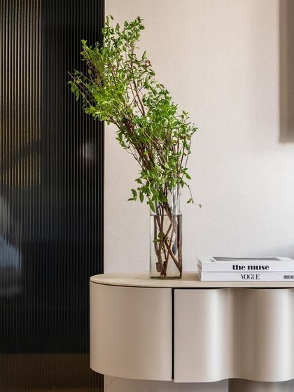 A close-up of the fluted glass pocket door and the elegantly curved console table. The fresh greenery adds a touch of life and color to the neutral palette.