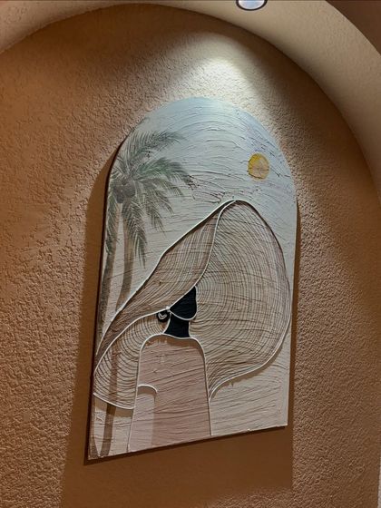 An art installation in an arched niche at Seezen cafe in Kanpur. This piece features a stylized figure with a large hat against a beachy, textured background.