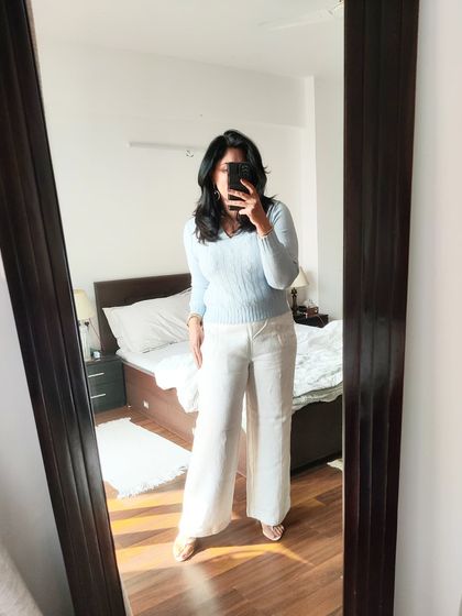 A mirror selfie showing the full look. Wide-leg linen pants are a summer staple, and they pair beautifully with a simple, lightweight sweater for a comfortable and stylish outfit.