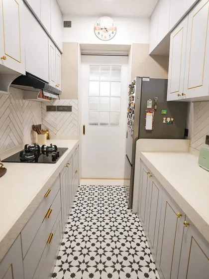 A minimalist black and white kitchen design. The patterned floor tiles add a bold graphic element, while the white cabinets with gold trim keep the space feeling bright and elegant.