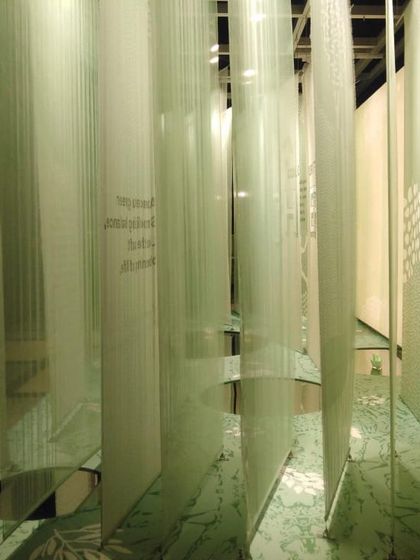 An immersive view of the 'Cherish' installation, where visitors walk through a forest of layered, printed fabrics. Pools of reflection on the floor mirror the installation, adding another layer of meaning to this experience of forest bathing.