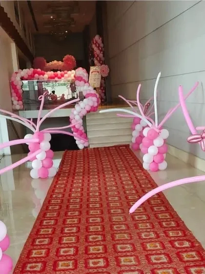 A grand hallway entrance decorated with pink and white balloon arches and columns. The red carpet leads guests into the main event space in style.