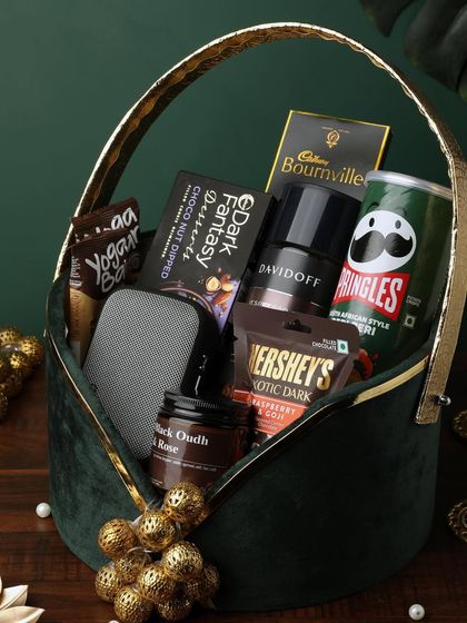 A luxurious green velvet basket overflowing with premium brands. This hamper includes Davidoff coffee, Pringles, Bournville, Hershey's, a portable speaker, and a black oudh and rose candle.