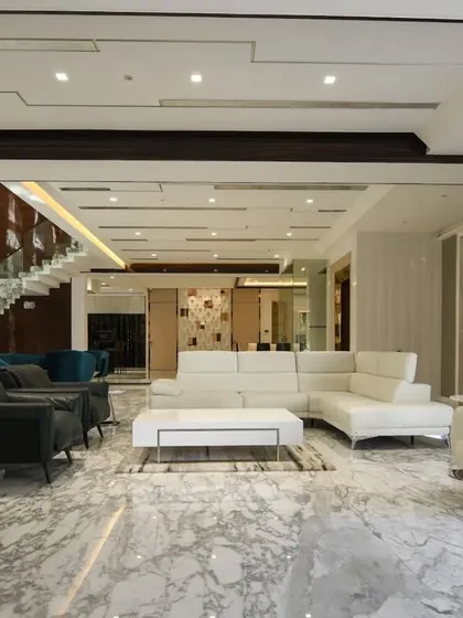 Luxury and spaciousness are defined by a cohesive design language. This living area features pristine marble floors, a crisp white sectional sofa, and recessed lighting, creating a sophisticated environment that feels both grand and inviting.