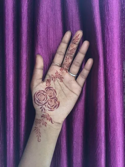 A delicate design featuring three small roses on the palm, with a light vine extending up the wrist and finger.