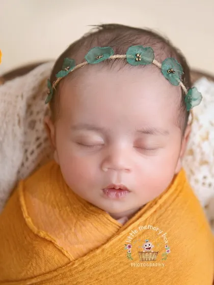 A close-up of this little one's face, showing the delicate green headband and their sweet, sleepy expression.