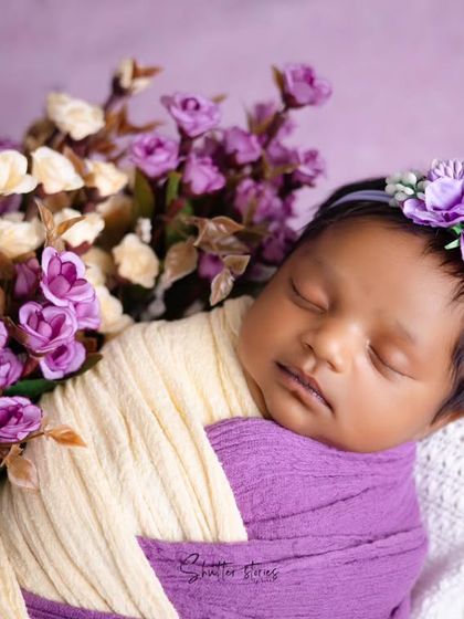 This portrait uses a complementary color scheme of purple and cream. The floral arrangement adds texture and frames the baby's face beautifully.
