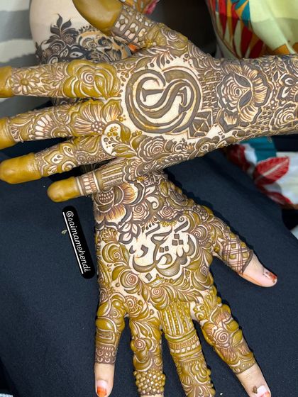 A beautiful top-down view of a completed bridal mehendi, featuring the initial 'S' and a name in script, showcasing the full, cohesive look.